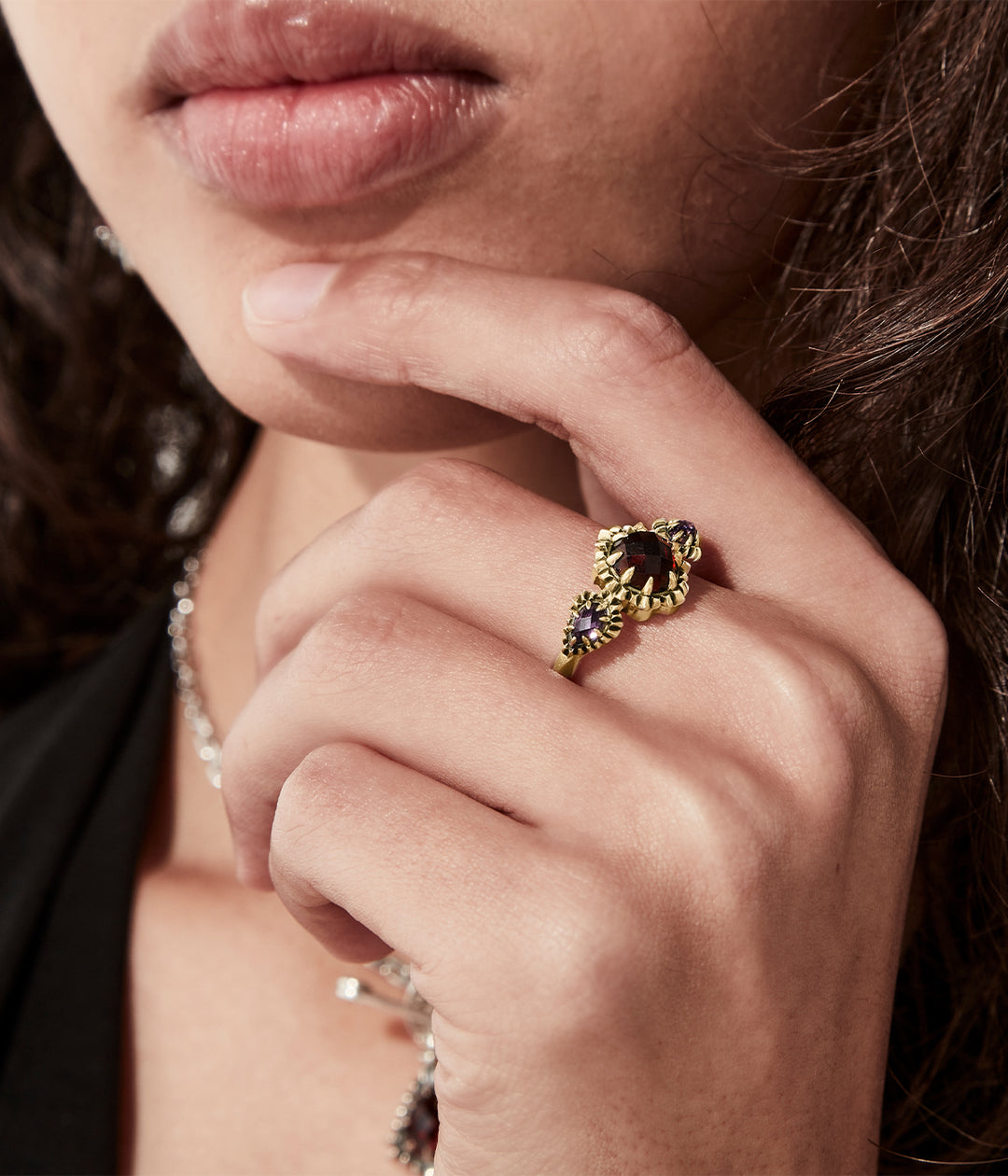 On-model view of gold triple gemstone ring on female hand, dark background