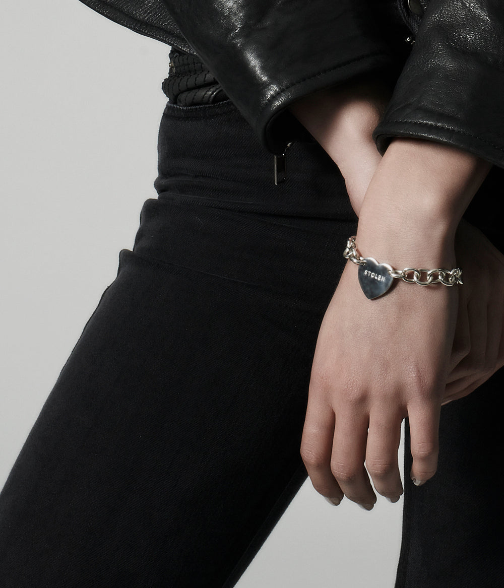 Female model wearing silver chain bracelet with heart charm, styled to show scale and movement.