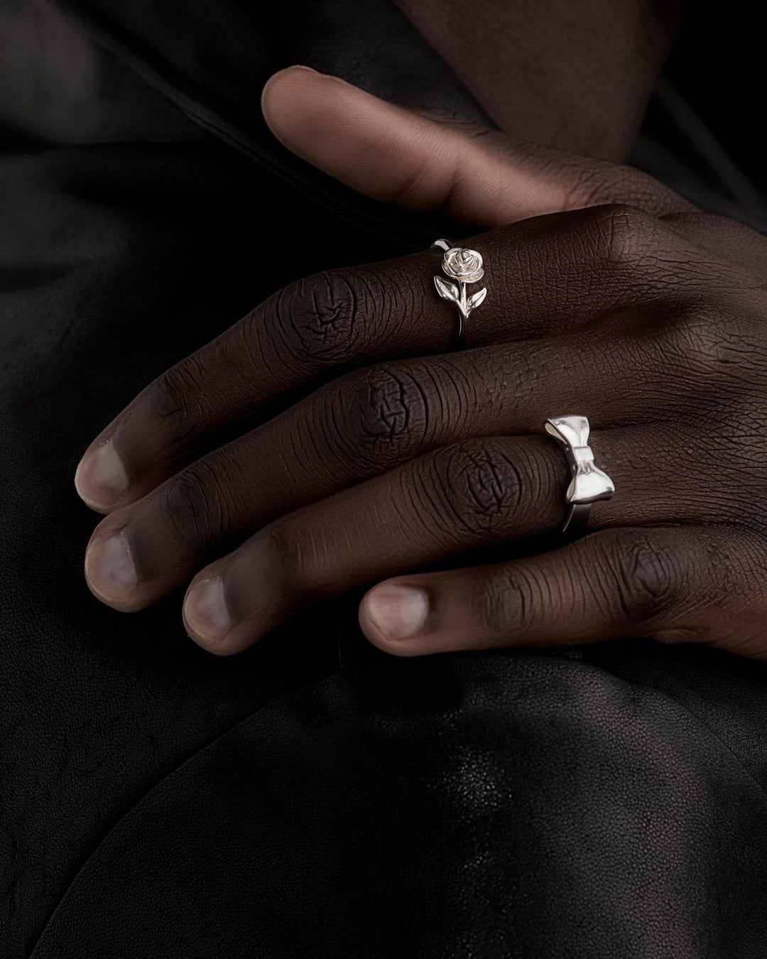 Stem Rose Ring styled on male model’s hand, shown close-up with Bow Ring, highlighting contrast in sculptural details against skin tone and natural light